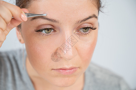 一位caucasian女人的近视肖像 她用tweezers做眉毛矫正自己喜悦镊子采摘女性护理女孩闲暇治疗工具疼痛图片