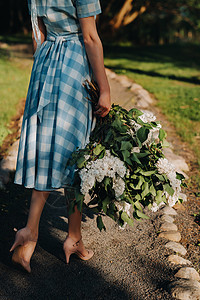 一个美丽的年轻模特女孩 穿着草帽在公园装扮 在桑尼春日带一束花束白开花的长袍图片