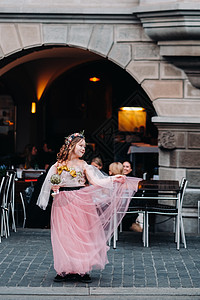 穿着小衣服一个穿着粉红色公主裙的小女孩手里拿着一束花穿过苏黎世老城 瑞士城市街道上一个穿着粉红色连衣裙的女孩的肖像头发花束童年街道乐趣公主背景