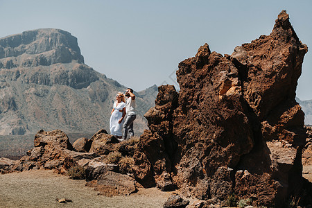 一个穿着白色衣服和眼镜的男人和一个女孩站在泰德火山的火山口 一对夫妇站在西班牙特内里费岛火山口的一座山上顶峰世界火山陨石游客公园图片