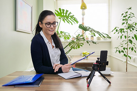 商业女性在寻找智能手机网络摄像头 在线聊天 录制视频教学顾问咨询笔记训练电子商务办公室互联网送货工作图片