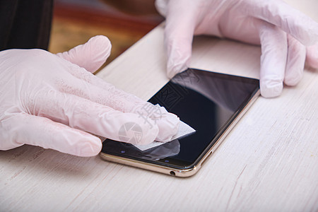 戴橡胶手套的男子用湿布擦擦他的智能手机玻璃 然后在保护杯上粘胶图片