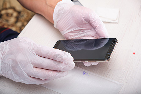 一个戴橡皮手套的男人拿着一个电话 他用屏幕上的新玻璃杯修理了一部电话图片