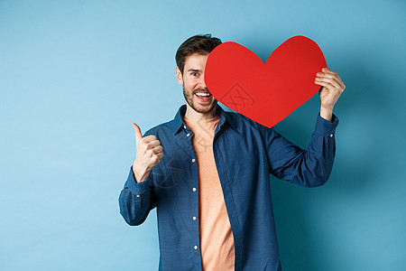 快乐的男人展示情人节的心和拇指举起手势 站在蓝背景上礼物假期丈夫情感胡子纪念日感情投标惊喜周年图片