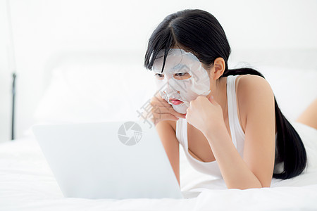 美丽的年轻亚洲女性 戴着面膜 躺在卧室床上的笔记本电脑上工作 美丽的女孩在家里用面膜进行皱纹护肤 护肤 健康和保健皮肤女士护理房图片