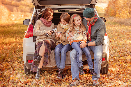 汽车女孩家庭坐在汽车后备箱中森林快乐树干叶子环境女孩父母女学生树叶姐姐背景
