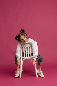 照片中微笑的小女孩被粉红背景所孤立牛仔裤乐趣学校白色喜悦椅子青春期假期女孩工作室图片