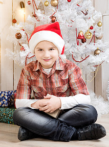 穿红帽子的小男孩 在新年树附近拿现装盒子儿子微笑花环工作室地面庆典帽子装饰礼物气氛图片