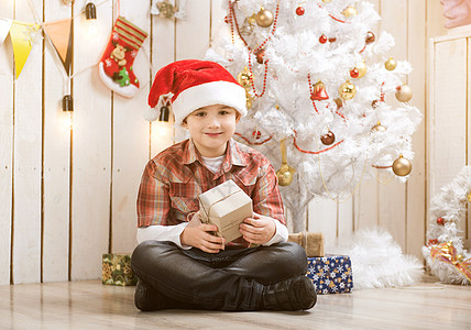 男孩坐在新年树旁边的地板上图片