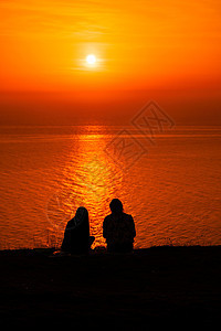 两个穿着可爱夏装的年轻女子坐在石头上 看着海面上金色的夕阳 复制空间 平静 沉默和与自然统一的概念图片