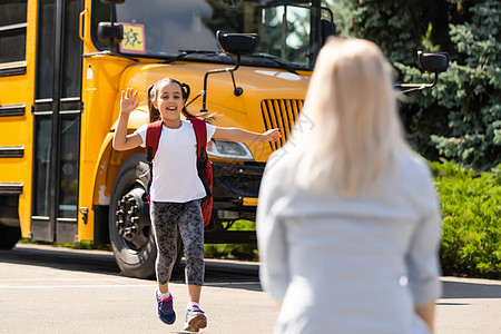 小孩学生在回到学校后 在校车附近碰见母亲亲手拥抱她跑步学习女儿们女士教育知识女儿乐趣会议中年图片