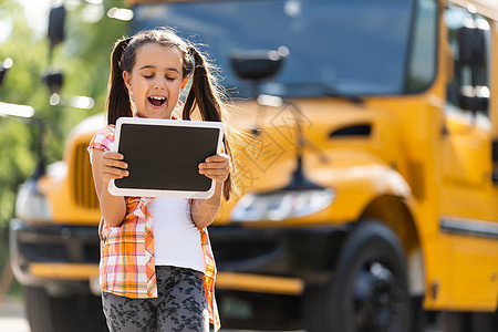 在校车附近看摄影机的 可爱的小女学生上学背包学习学校幸福汽车公共汽车青少年微笑车辆图片