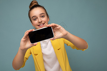 美丽微笑的少女照片看起来漂亮 穿着休闲时尚的服装 站在背景中 复制空间拿着智能手机 手里拿着手机 屏幕显示空 用于模拟看相机图片