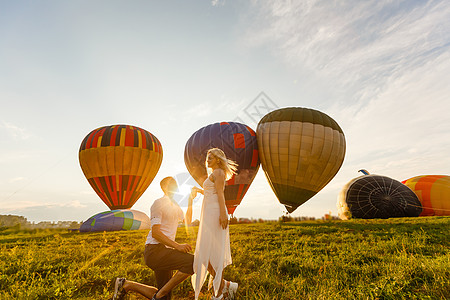 美丽的浪漫情侣拥抱在草地上 背景的热气球生长高度航程男人空气乐趣篮子航班美化奢华图片