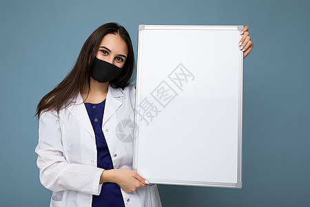 身穿白色医疗大衣和面罩的女医生 戴着空白板 有在背景上隔绝文字的复制空间Corona病毒概念医师磁板防护外套面具女士药品小样护士图片