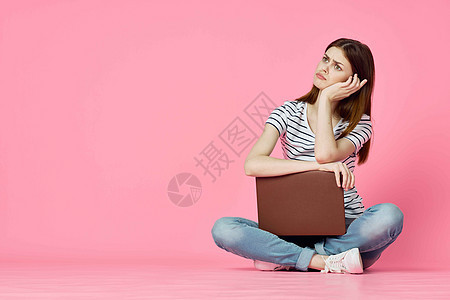 带着笔记本电脑的快乐女人 坐在粉红背景的地板上青少年技术互联网微笑学生粉色学习女士女孩学校图片