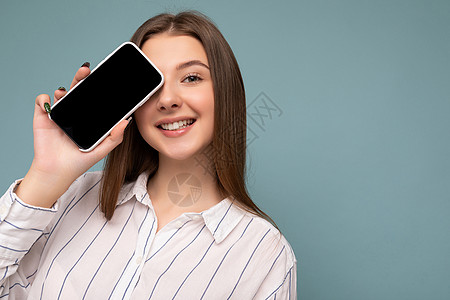 美丽微笑的年轻女子的特写照片 看起来漂亮 穿着休闲时尚的服装 站在背景上孤立 复制空间拿着智能手机 手拿手机 空屏幕显示 用于模图片