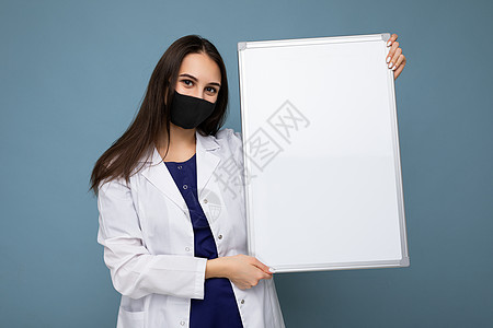身戴保护面罩和白色医疗大衣的年轻护士 带着蓝色背景隔离的空磁板以及药品医生保健感染医师外套小样肺炎空间卫生图片