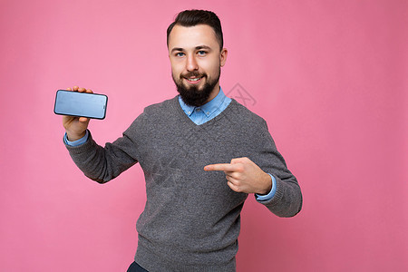 照片中 英俊微笑的成年男性长相英俊 穿着休闲装 站在背景中与世隔绝 复制空间拿着智能手机 手里拿着手机 屏幕显示为空屏幕 用于模图片