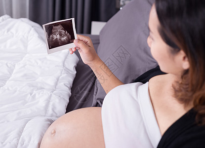 具有超声波图像的孕妇 婴儿坐在家中卧室的床上母性闲暇保健卫生公寓房子扫描怀孕母亲生活图片