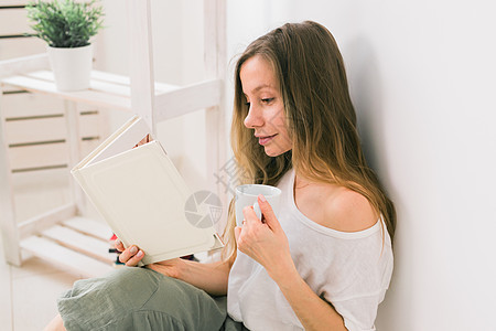 年轻女性在家里看相册 喝茶 回忆和闲暇的理念家庭照片阅读摄影女孩微笑专辑幸福享受喜悦图片