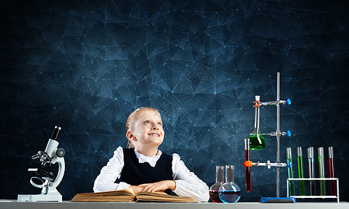 微笑的小女孩坐在书本开着的桌子上学生教育科学家知识学习瞳孔化学孩子学校测试图片
