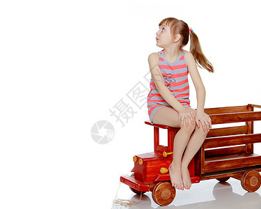 这女孩坐在一辆大的玩具木制汽车上冒充快乐机器木头女性微笑童年运输女儿车辆图片