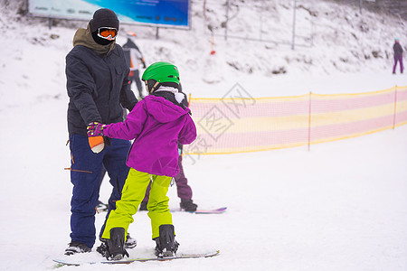 教官在雪坡向雪板上教导一名儿童滑雪板季节乐趣单板蓝色假期训练女儿自由父亲图片