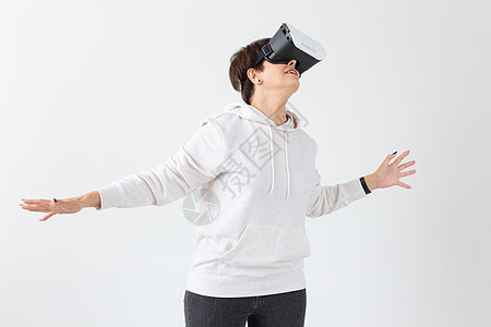 穿着轻毛衣的不明身份中年妇女玩3D游戏 在白色背景上戴虚拟现实眼镜 针对老年人的高科技概念 高科技快乐成人黑发女士微笑女性发型喜图片