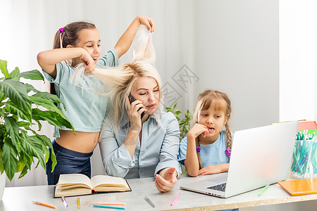 一位有两个孩子的年轻母亲在家里用电脑工作 疲劳生活方式家庭主妇自由职业者 疲乏的母亲和两个小女儿技术女孩孩子们儿子商业父母互联网图片