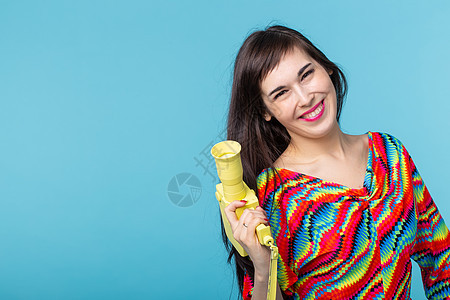 一个微笑的年轻女子的画像 她手里拿着一台老式黄色摄像机 在蓝色背景下摆姿势 视频和摄影的概念女孩成人魅力快乐潮人黑发身体衣服艺术图片