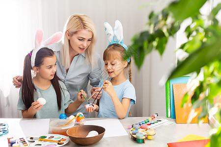 年轻母亲和两个小女儿在家里画彩色复活节鸡蛋 在家中绘画学校女士学习孩子庆典活动妈妈装饰品姐姐婴儿图片