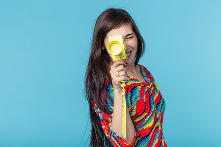 一个微笑的年轻女子的画像 她手里拿着一台老式黄色摄像机 在蓝色背景下摆姿势 视频和摄影的概念成人女孩魅力黑发衣服快乐潮人女性艺术图片