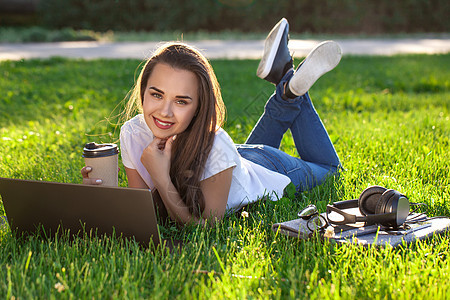 年轻女性在公园里使用笔记本电脑 躺在绿草地上 休息时间活动概念闲暇快乐成人技术阳光大学学生乐趣幸福微笑图片
