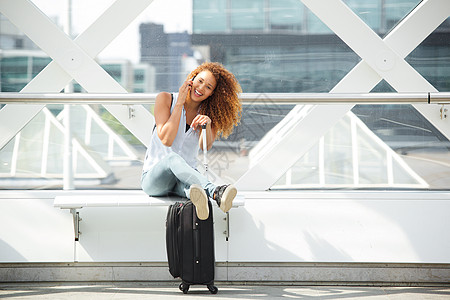 听你说快乐的旅行妇女坐着行李箱 在车站上接听手机背景
