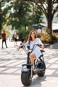 年轻美丽的年轻女子和一辆电动摩托车 生态运输工具街道闲暇城市运输女士女孩车辆乐趣女性技术图片