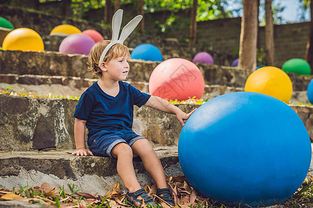 可爱的小男孩 长着兔耳朵 在户外玩传统的复活节彩蛋 庆祝复活节假期 蹒跚学步的发现 五颜六色的鸡蛋乐趣篮子孩子阳光公园团体太阳婴图片