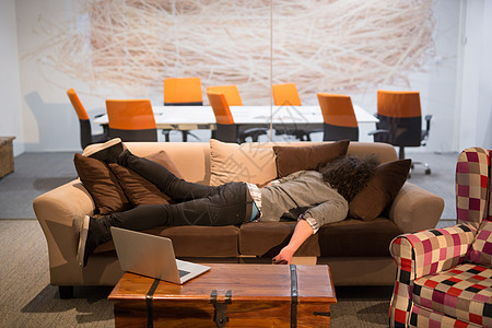 男人睡在有创意的办公室的沙发上职业桌子经理睡眠笔记本男性压力职场电脑技术图片