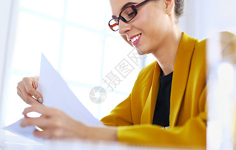 漂亮的年轻女商务人士坐在笔记本电脑前的办公桌前做一些文书工作桌子手机职业办公室工作站讨论人士眼镜顾问微笑图片