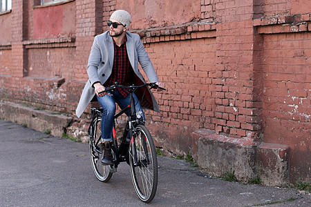 穿着灰色大衣和帽子的帅哥年轻人 在城里骑自行车街享受外套街道商务工作男人男性游客机动性公司图片