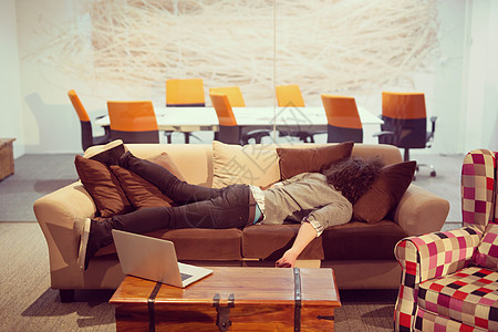 男人睡在有创意的办公室的沙发上管理人员桌子经理说谎电脑职业睡眠男性压力工人图片