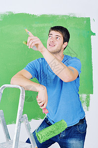 英俊的青年男子用彩色漆白白墙财产刷子男性职业装潢微笑维修工人工匠房间图片