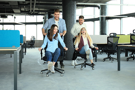 年轻快乐的商务人士穿着智能便衣 玩得开心 一边在办公室椅子上赛车 一边笑着笑手势休闲活动业务庆典成人情绪休息商务移动图片