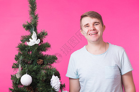 人 假期和圣诞节概念  粉红色背景中靠近圣诞树的年轻微笑男子工作室闲暇毛衣庆典男性幸福情绪快乐新年男人图片