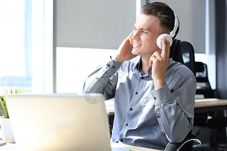 在现代办公室用耳机吹嘘和聆听音乐 微笑着英俊的商务人士工人经理工作休息教育技术管理人员企业家商务地点图片