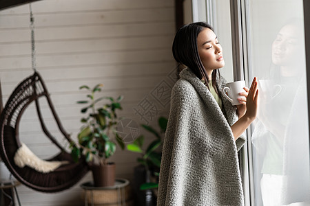 拿着杯子的女孩年轻年青的亚洲女孩坐在窗户旁边的家里 用怀旧的渴望的脸面向外面 拿着杯子和热饮发烧疾病女性感染卫生疼痛房子肺炎毯子互联网背景