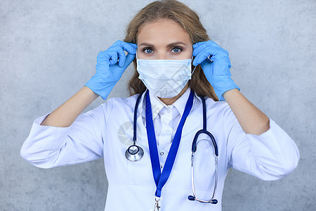 戴医疗面具的女医生 带着听诊器 看着在灰色背景上隔绝的照相机实验室外套医院职业从业者女士护士推杆工人手套图片
