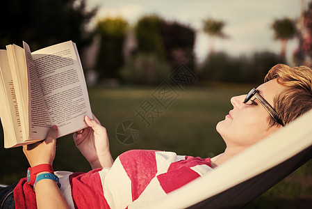 女人一边看书 一边放松吊床假期花园天堂闲暇成人日落女性旅行小说享受图片
