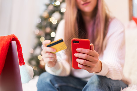 特写有手机 信用卡和膝上型计算机的妇女 圣诞节假期在线购物 女孩从家里发短信 圣诞快乐 新年快乐 圣诞树图片