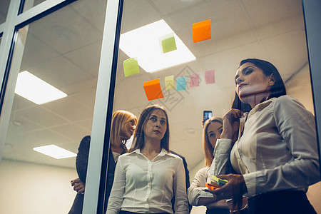 青年自由职业者小组使用在玻璃墙上张贴的贴纸 在创造性办公室就想法和沟通开展工作 并共同进行交流;成功的团队概念 (A/C 5/4图片